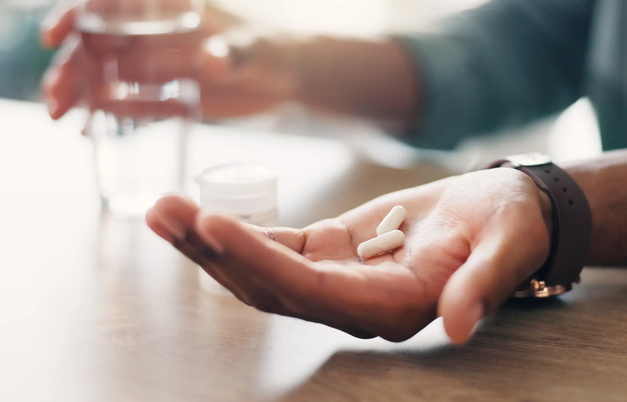Hand holding two white capsules and water
