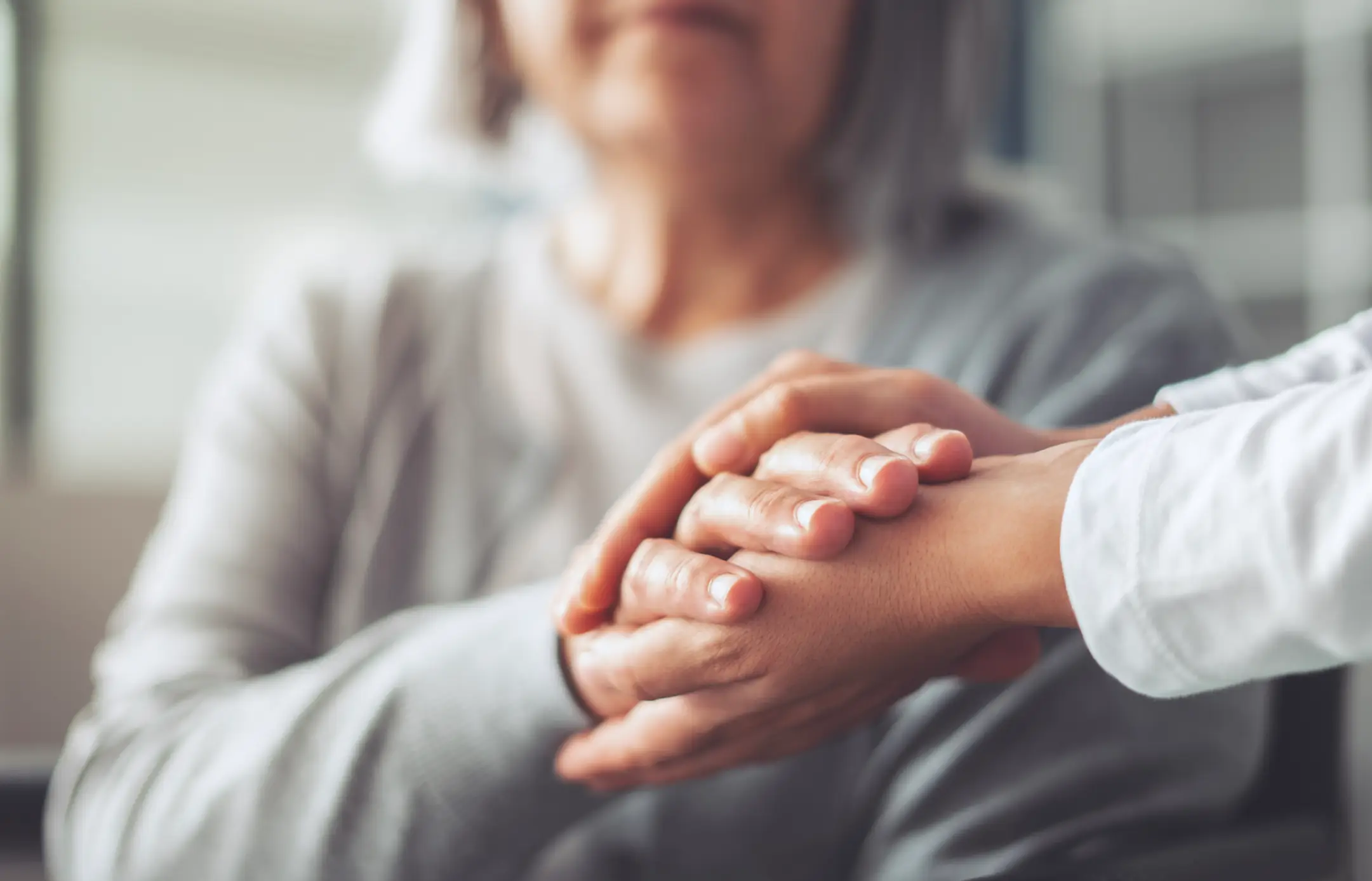 Caregiver comforting elderly person by holding hands